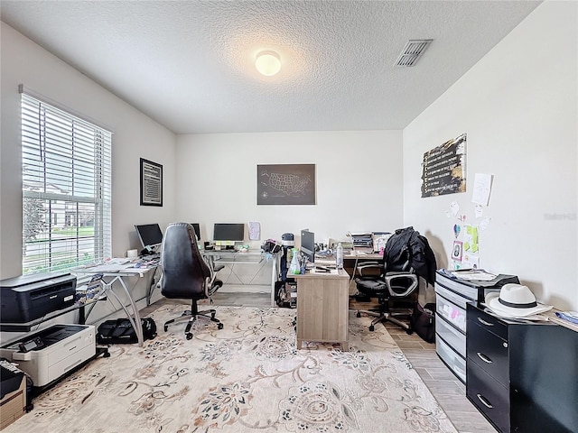 home office featuring light wood-style floors, visible vents, and a textured ceiling