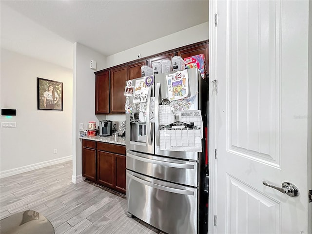 kitchen featuring baseboards, light stone counters, dark brown cabinets, light wood-type flooring, and stainless steel refrigerator with ice dispenser