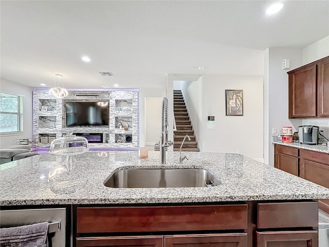 kitchen featuring a kitchen island with sink, a sink, visible vents, and light stone countertops