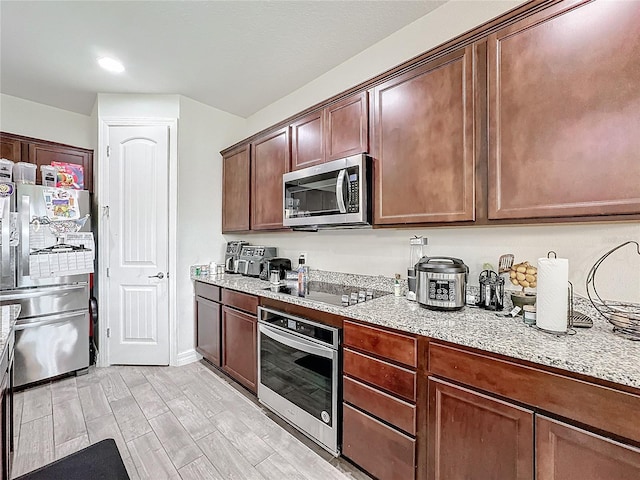 kitchen with appliances with stainless steel finishes, light wood-type flooring, and light stone counters