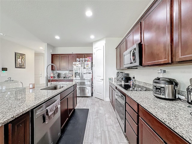 kitchen featuring light wood finished floors, appliances with stainless steel finishes, light stone countertops, a textured ceiling, and a sink