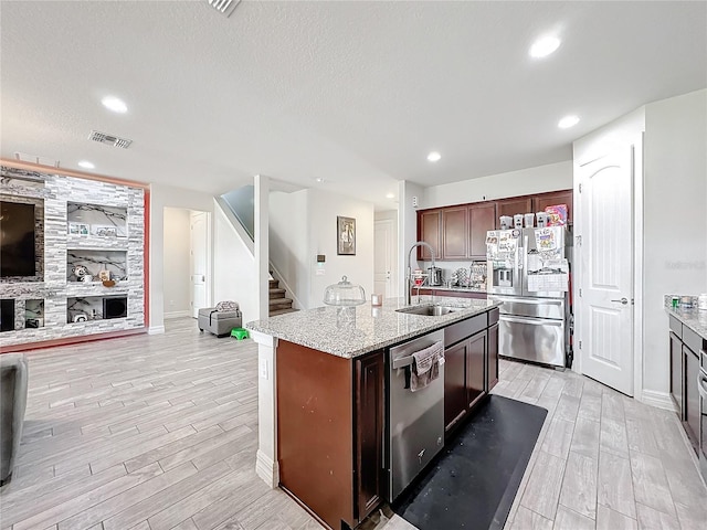 kitchen featuring appliances with stainless steel finishes, wood finish floors, a sink, and an island with sink