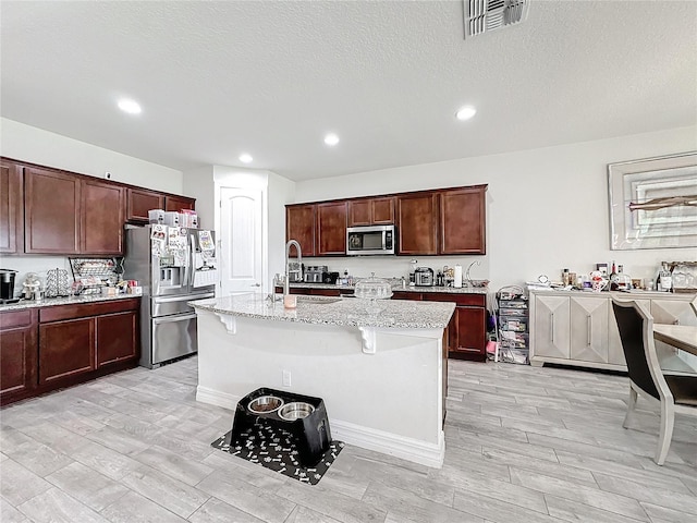 kitchen featuring light stone counters, a breakfast bar area, stainless steel appliances, visible vents, and an island with sink