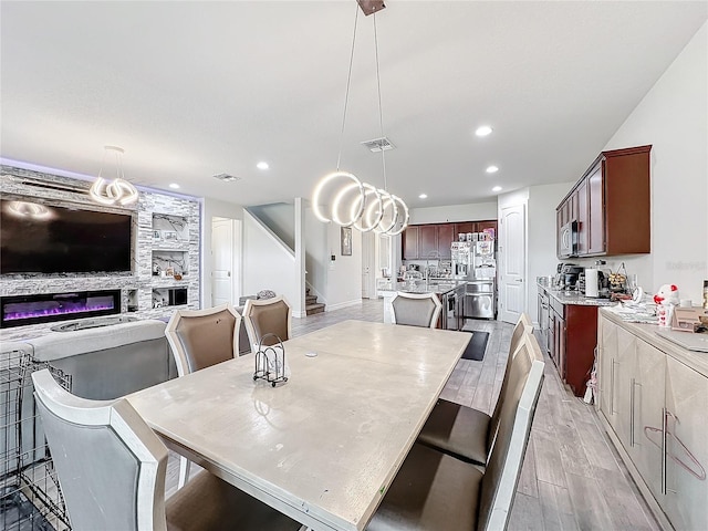 dining space with visible vents, a glass covered fireplace, light wood-style flooring, stairs, and recessed lighting