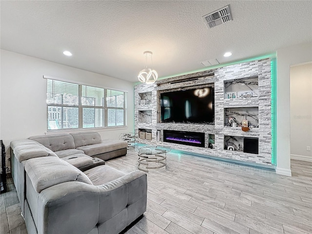 living area featuring baseboards, visible vents, a textured ceiling, light wood-style floors, and a fireplace