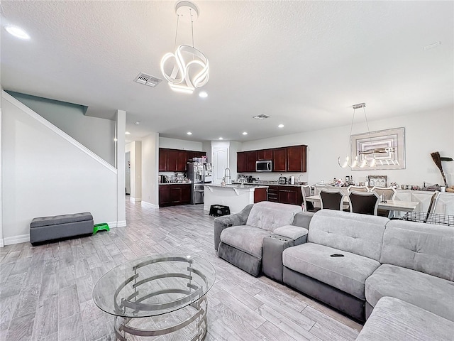 living area featuring visible vents, light wood-style flooring, a textured ceiling, and an inviting chandelier