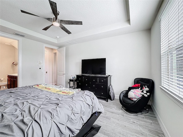 bedroom with light wood-type flooring, a textured ceiling, visible vents, and a tray ceiling