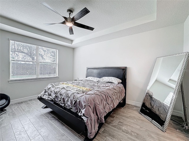 bedroom with light wood finished floors, baseboards, a tray ceiling, and a textured ceiling