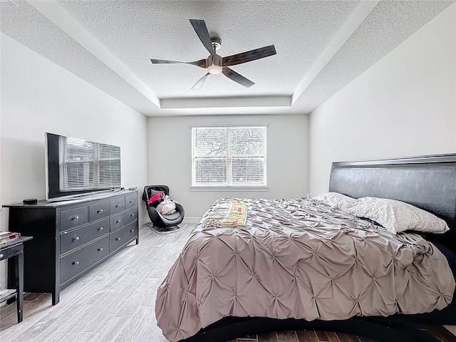 bedroom featuring a textured ceiling, a raised ceiling, a ceiling fan, and light wood-style floors