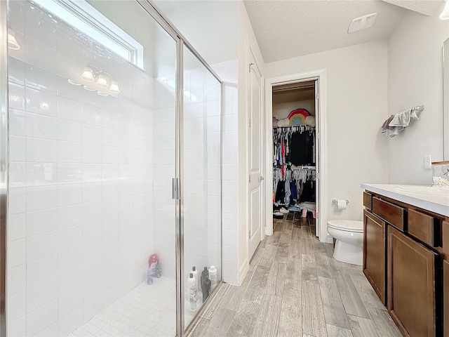 full bathroom with visible vents, a spacious closet, a stall shower, a textured ceiling, and wood finished floors