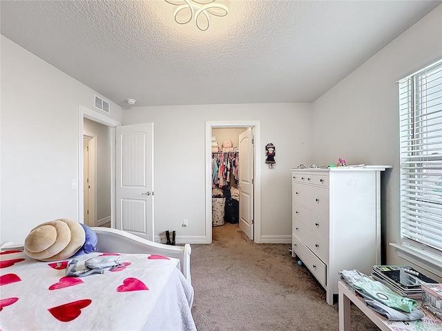 bedroom with a walk in closet, light colored carpet, visible vents, a textured ceiling, and baseboards