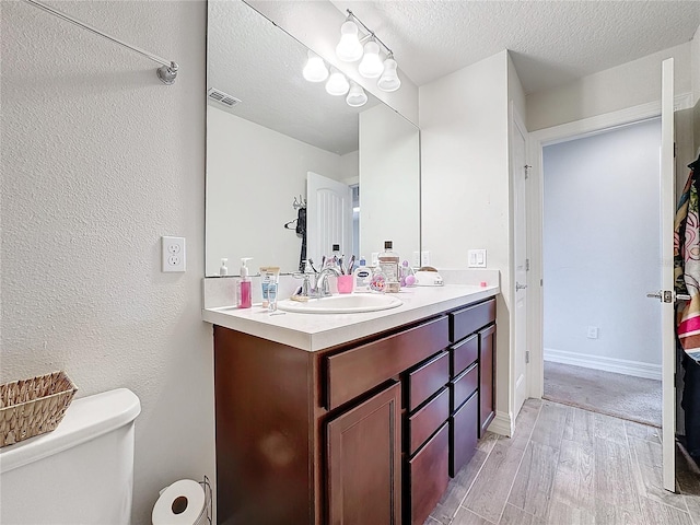 bathroom with visible vents, toilet, wood finished floors, a textured ceiling, and vanity