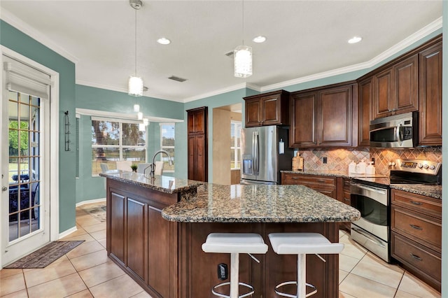 kitchen with pendant lighting, a center island with sink, appliances with stainless steel finishes, dark stone countertops, and dark brown cabinets