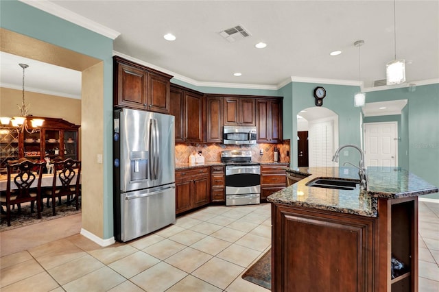 kitchen featuring stainless steel appliances, a sink, visible vents, dark stone countertops, and decorative light fixtures