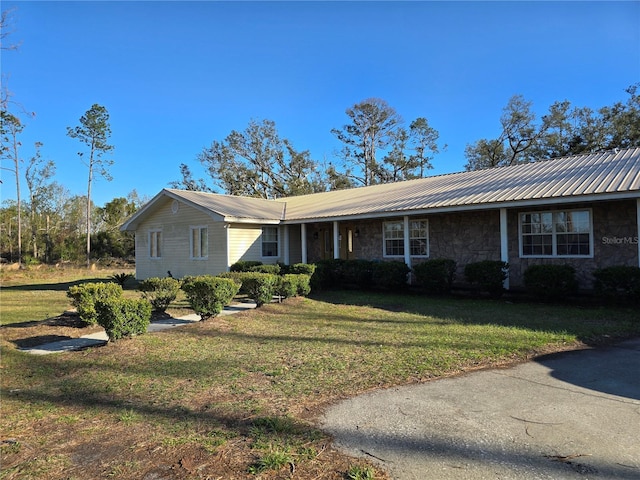 ranch-style house with metal roof, stone siding, and a front yard