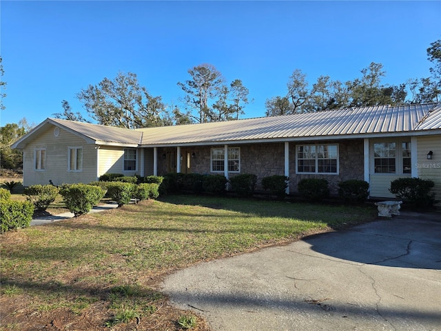 ranch-style home with stone siding, metal roof, and a front lawn