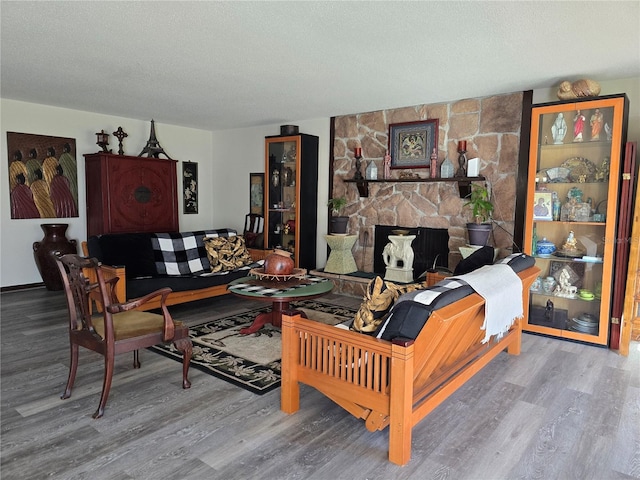 living area with a textured ceiling, a stone fireplace, and wood finished floors