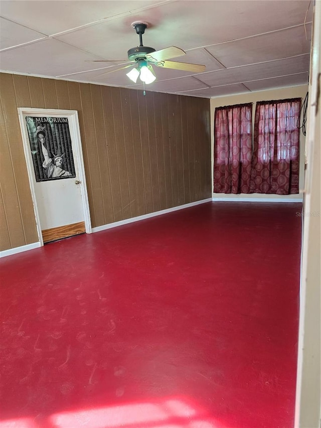 spare room with concrete flooring, wooden walls, baseboards, and a ceiling fan