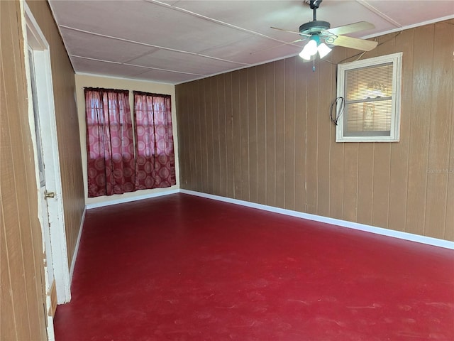 unfurnished room with ceiling fan, wooden walls, concrete flooring, and baseboards