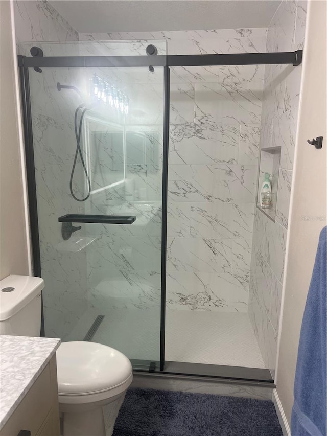 bathroom featuring a marble finish shower, vanity, and toilet