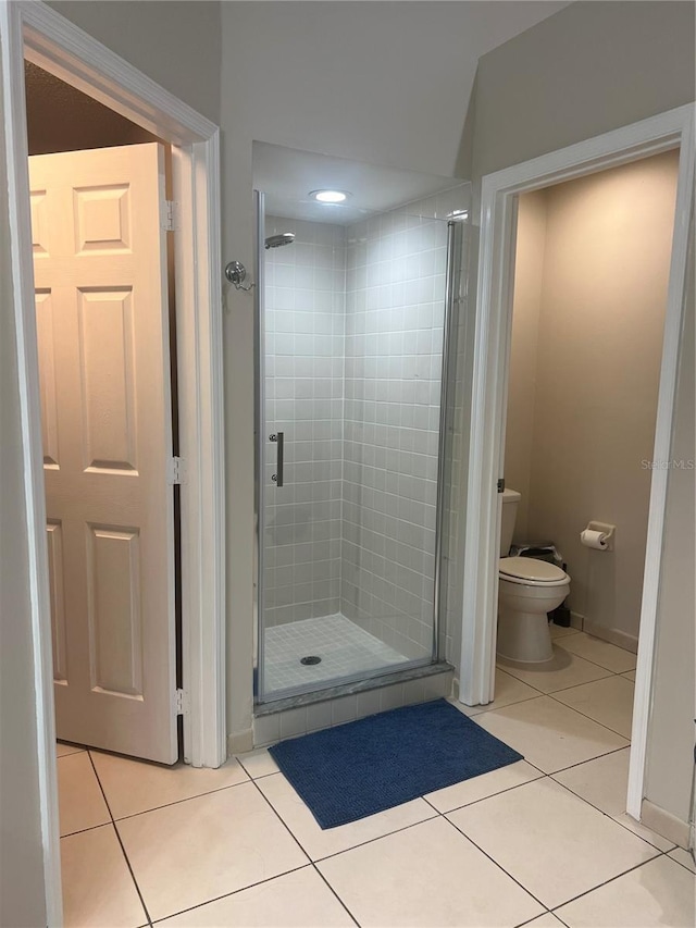 bathroom with toilet, a stall shower, tile patterned flooring, and baseboards