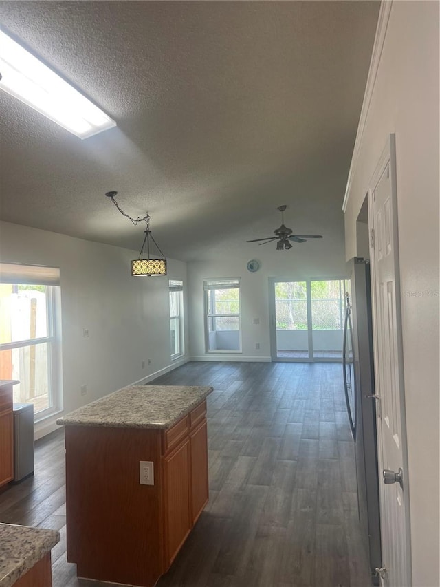 kitchen with a textured ceiling, vaulted ceiling, brown cabinets, dark wood finished floors, and decorative light fixtures