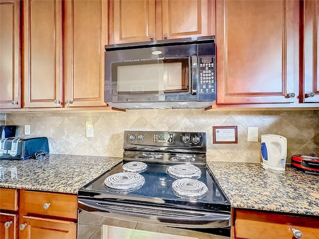 kitchen with a toaster, black appliances, tasteful backsplash, brown cabinetry, and dark stone countertops