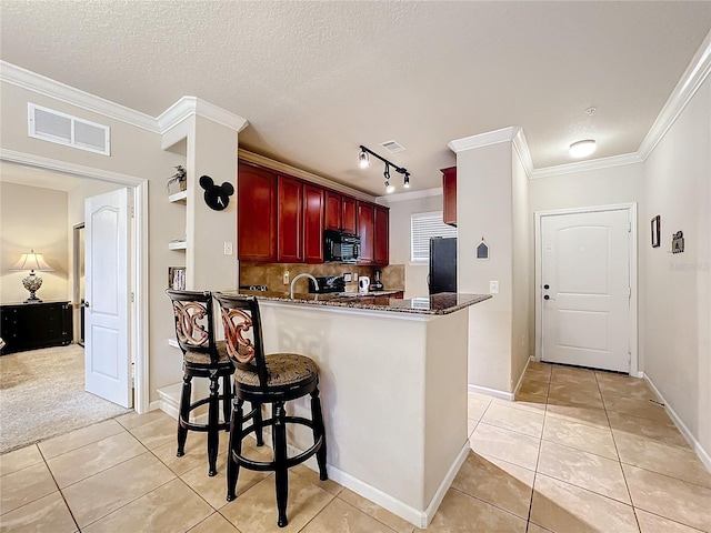 kitchen with black microwave, a peninsula, visible vents, reddish brown cabinets, and dark stone countertops