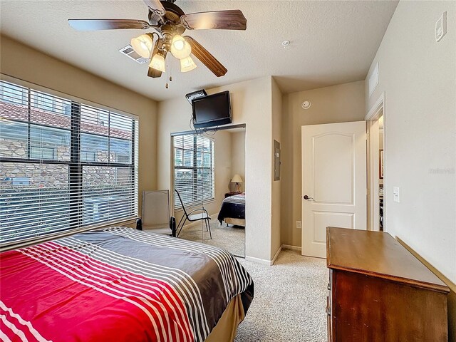 bedroom with ceiling fan, baseboards, a textured ceiling, and light colored carpet