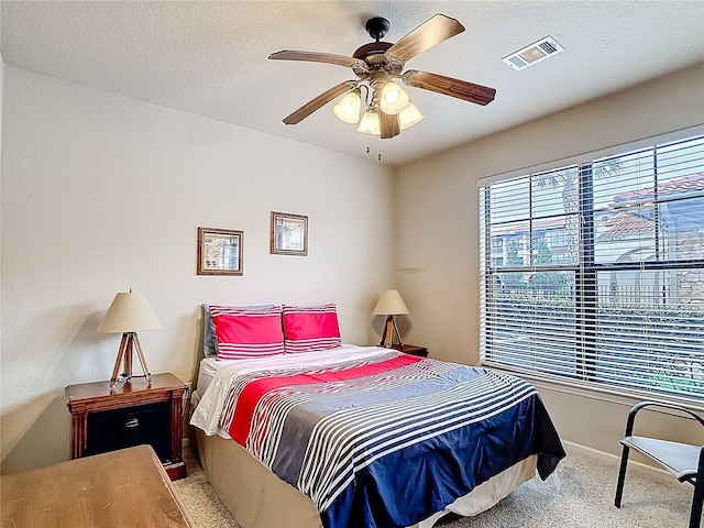 bedroom featuring light colored carpet, visible vents, a ceiling fan, a textured ceiling, and baseboards