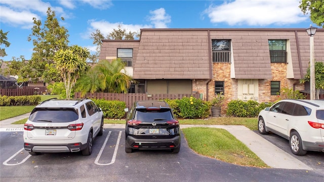 multi unit property with uncovered parking, brick siding, mansard roof, and fence