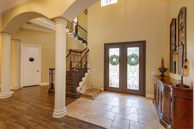 foyer entrance featuring decorative columns, a towering ceiling, baseboards, french doors, and stone tile flooring