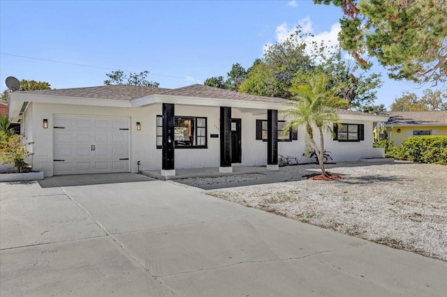 ranch-style house featuring a garage, concrete driveway, roof with shingles, and stucco siding