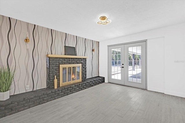 unfurnished living room with french doors, a brick fireplace, and wood finished floors