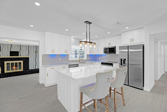 kitchen with light stone counters, stainless steel appliances, a sink, a center island, and decorative backsplash