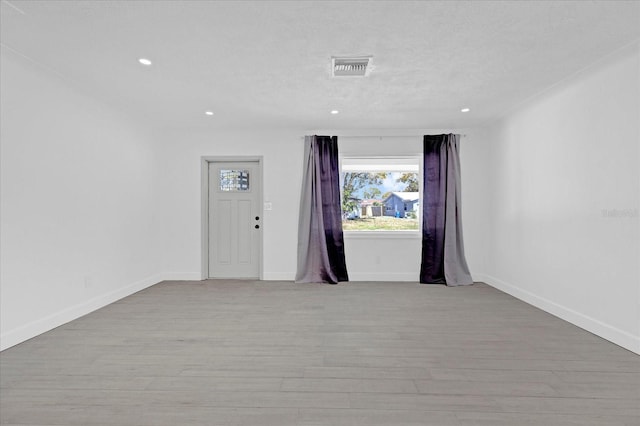 unfurnished room featuring visible vents, a textured ceiling, baseboards, and wood finished floors