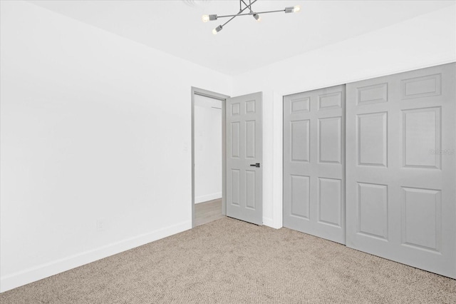 unfurnished bedroom featuring an inviting chandelier, a closet, baseboards, and carpet flooring