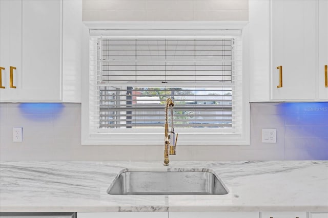 kitchen with light stone counters, white cabinets, a sink, and decorative backsplash