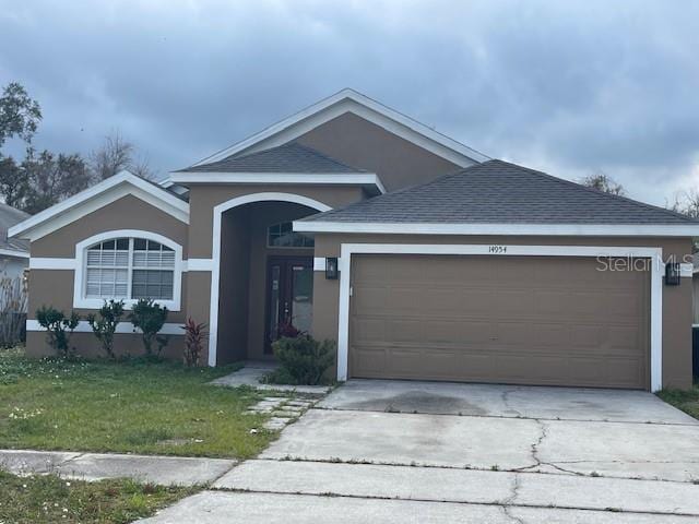 ranch-style house with a garage, concrete driveway, a front yard, and stucco siding