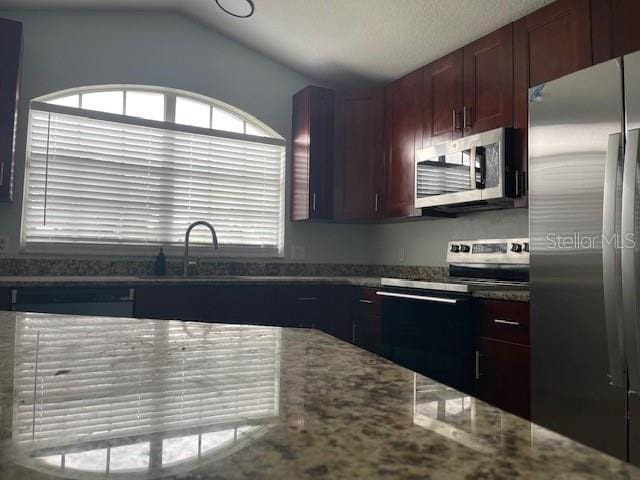 kitchen featuring appliances with stainless steel finishes, vaulted ceiling, a sink, and light stone countertops