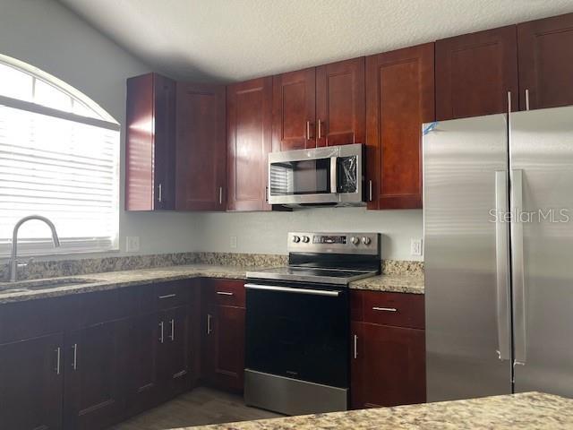 kitchen featuring reddish brown cabinets, stainless steel appliances, a sink, and light stone countertops