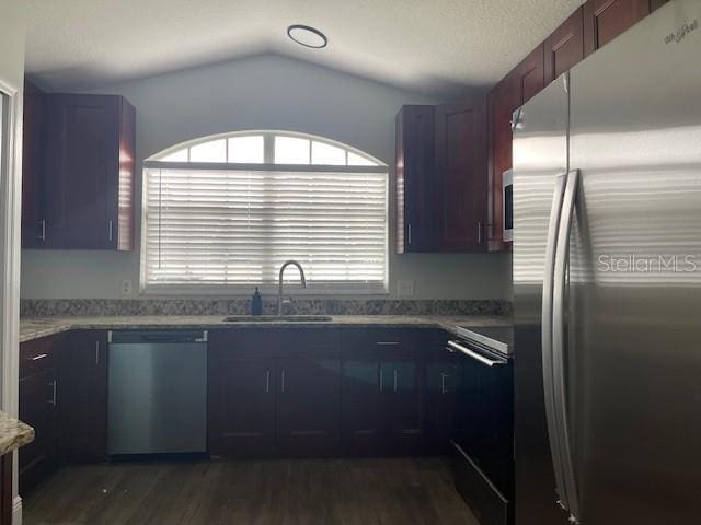 kitchen with lofted ceiling, stone countertops, dark wood-style flooring, a sink, and appliances with stainless steel finishes