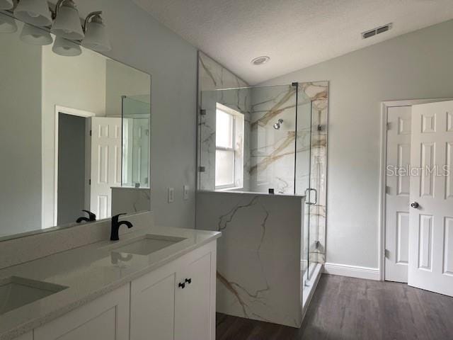 full bathroom featuring a marble finish shower, double vanity, lofted ceiling, visible vents, and wood finished floors