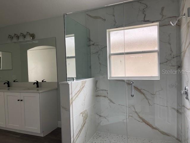 full bathroom featuring double vanity, a marble finish shower, and a sink