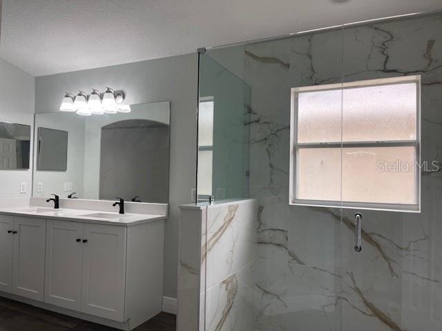 full bath with a sink, double vanity, and a marble finish shower