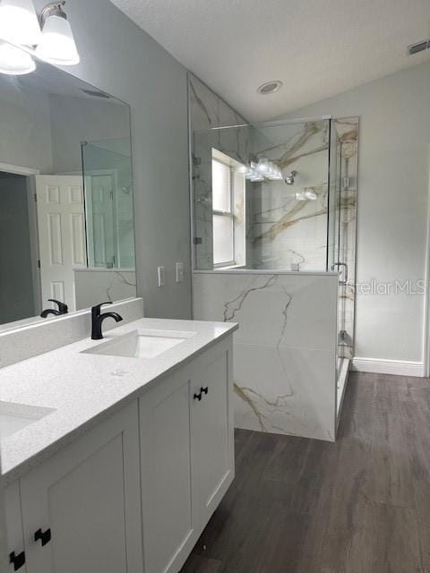 bathroom with double vanity, a marble finish shower, visible vents, wood finished floors, and a sink