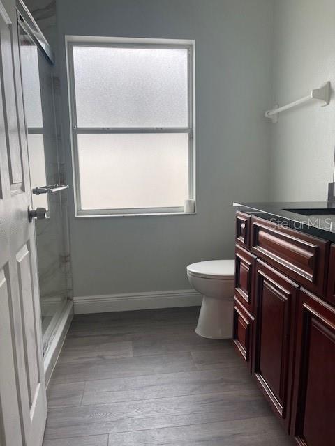 full bathroom featuring baseboards, a shower stall, toilet, and wood finished floors