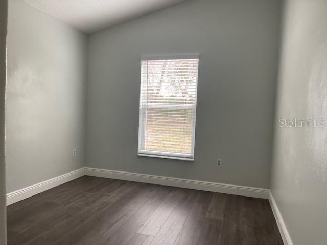 empty room featuring vaulted ceiling, dark wood-type flooring, and baseboards