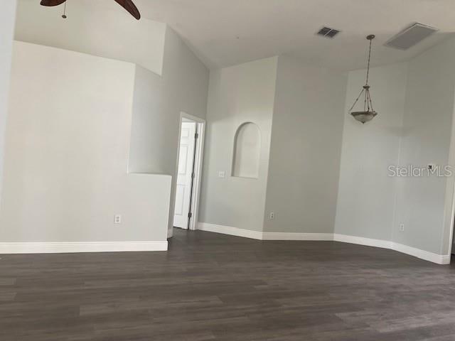 empty room featuring visible vents, dark wood finished floors, baseboards, and ceiling fan