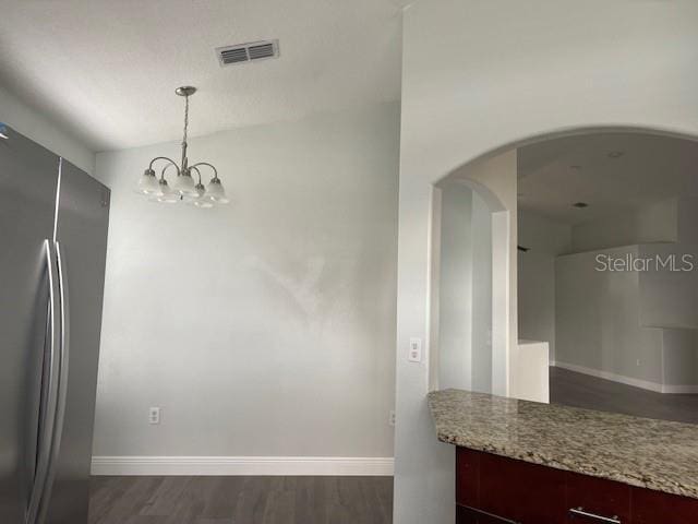 unfurnished dining area featuring arched walkways, dark wood finished floors, visible vents, and baseboards